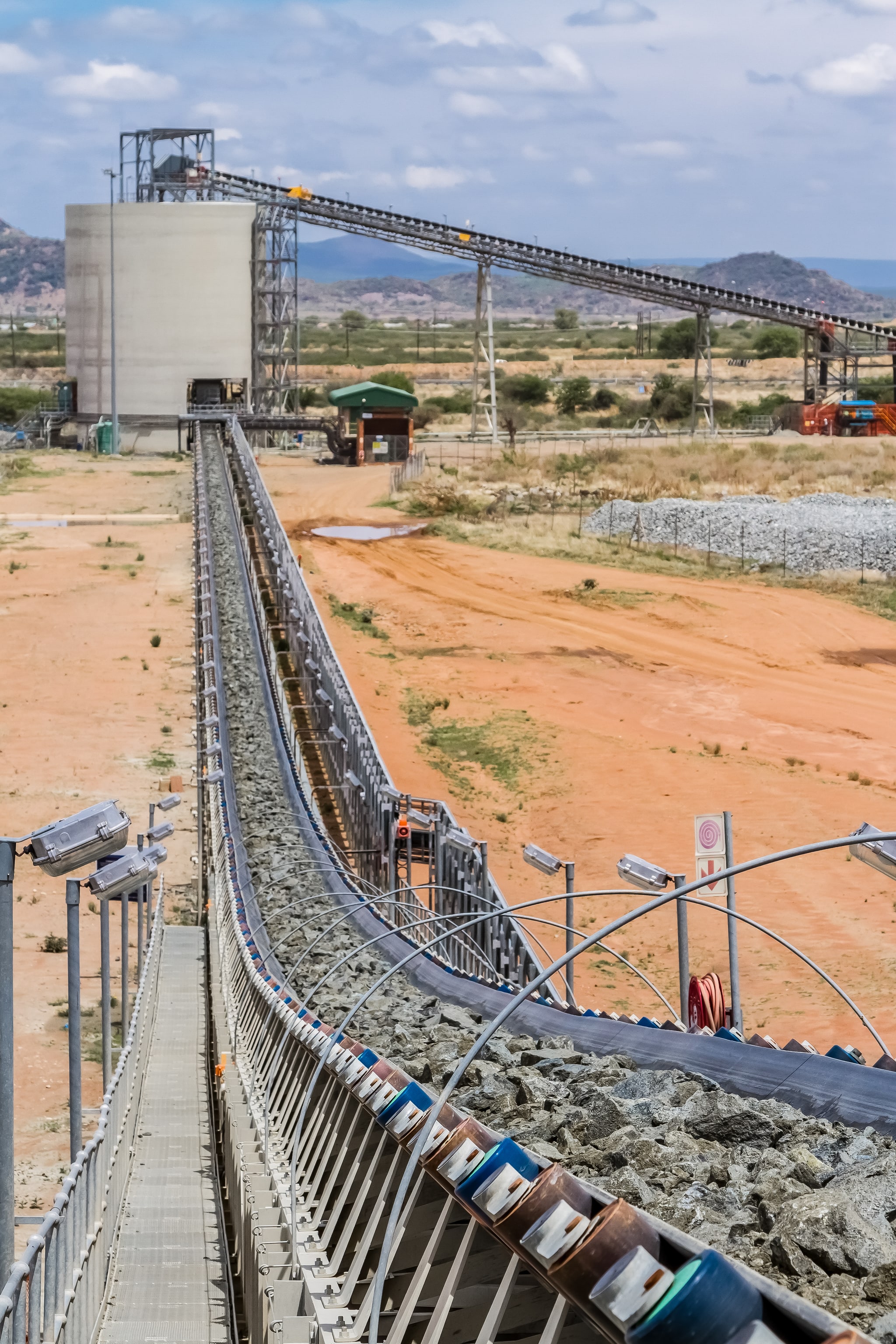 Conveyor carrying crushed ore toward a mineral processing plant silo across an open mining site
